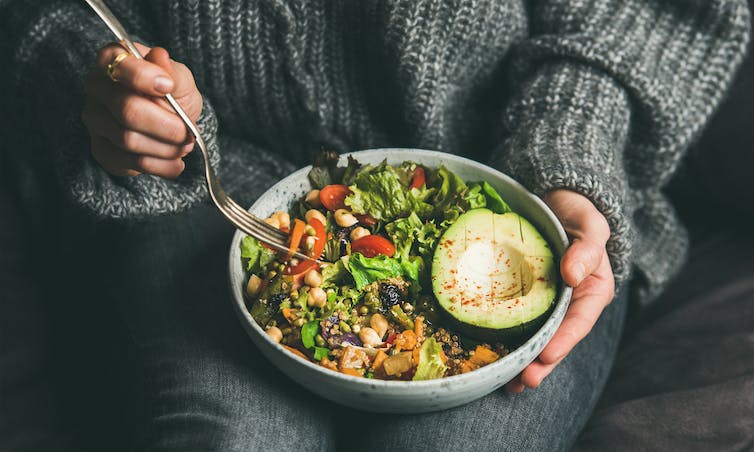 Mujer comiendo plato vegano de ensalada.